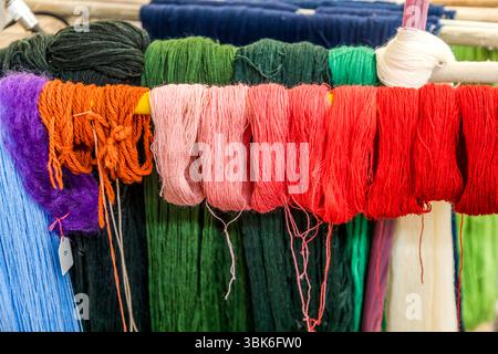 Gomitoli di lana tinti di viola, arancione, rosa, rosso, verde, blu e bianco pendono su pali di legno per asciugare nell'officina di tintura della filanda Terrade (Filature Terrade) in Rue de la Papeterie a Felletin vicino ad Aubusson, Creuse, Nouvelle-Aquitaine, Francia. Le sfumature rosse vanno dal rosa pallido al rosso scuro. Il processo di tintura si basa generalmente su un campione del cliente. Le tonalità desiderate sono create da tre colori base in forma di polvere e da un'attenta osservazione. Tutte le ricette si basano sull'esperienza, non su istruzioni scritte. L'intensità del colore dipende da quanto tempo il filo rimane nel bagno di tintura Foto Stock