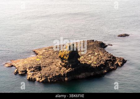 Una piccola isola con una roccia adagiata in mezzo all'oceano. L'acqua è calma e il cielo è limpido Foto Stock
