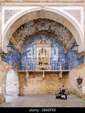 Busker che suona la chitarra acustica, la storica porta principale del castello di Óbidos, porta da Vila, decorata con piastrelle blu e bianche, architettura portoghese Foto Stock