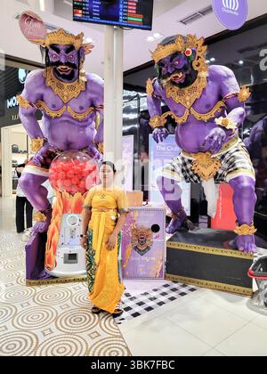 Giovane donna che indossa un sari giallo di fronte a due statue mitologiche viola all'aeroporto internazionale di Bali, Indonesia Foto Stock