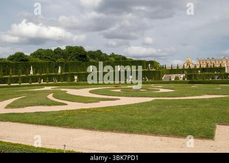 Giardino formale con sentieri di ghiaia, siepi curate, sculture e il palazzo visibile sullo sfondo sotto un cielo nuvoloso al Palazzo di Vers Foto Stock