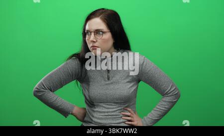 Donna con occhiali mostra espressioni su uno sfondo verde brillante indossando un maglione grigio che cattura l'emozione e la bellezza naturale Foto Stock