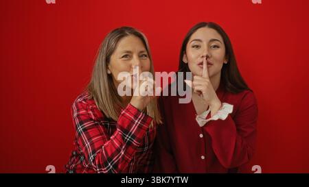 Madre e figlia condividono un momento tranquillo e amorevole su uno sfondo rosso audace, mettendo in risalto il loro legame familiare e il loro patrimonio ispanico. Foto Stock