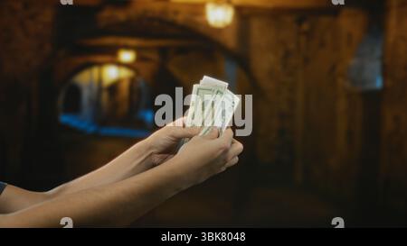 Uomo che tiene dollari americani all'aperto in una strada cittadina, concentrandosi su mani e banconote, catturando un'atmosfera urbana di scambio finanziario durante la notte Foto Stock