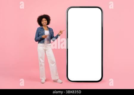 Allegra giovane donna afroamericana che punta a grande smartphone con schermo vuoto Foto Stock