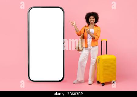 App prenotazione. Black Tourist Woman con valigetta che punta allo smartphone Big Blank Foto Stock