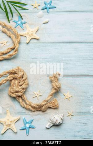 Decorazioni marine estive con foglie di palma, conchiglie, stelle marine e corda nautica adagiate su tavole di legno azzurre Foto Stock