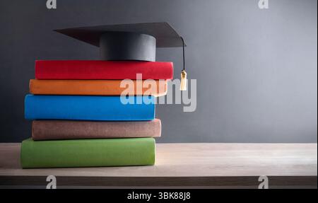 Concetto di laurea e istruzione con bacheca su una pila di libri con spine multicolore su un tavolo di legno e sfondo scuro isolato. Vista frontale Foto Stock