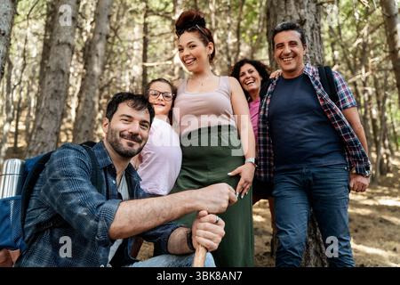Un grande, felice e variegato gruppo di amici o familiari si posa per una foto mentre camminano insieme in una foresta soleggiata Foto Stock