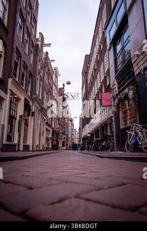 Le strade di Amsterdam, fiancheggiate da bellissime case colorate, vari caffè e pub, con biciclette parcheggiate lungo il tragitto. Foto Stock