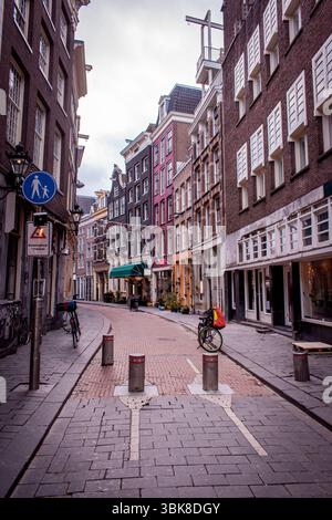 Le strade di Amsterdam, fiancheggiate da bellissime case colorate, vari caffè e pub, con biciclette parcheggiate lungo il tragitto. Foto Stock