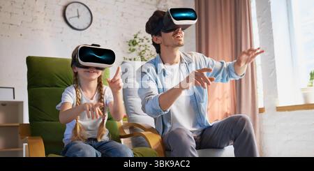 Padre e figlia si godono l'esperienza di realtà virtuale nel salotto moderno Foto Stock