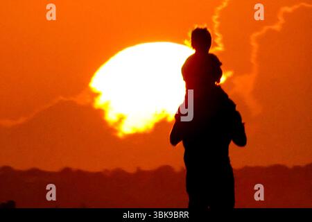 Isola di Palms, Stati Uniti. 19 giugno 2025. Un padre porta suo figlio sulle spalle mentre si fermano a guardare l'alba in una mattina calda e umida a Front Beach, il 19 giugno 2025, a Isle of Palms, Carolina del Sud. Un'enorme cupola di calore coprirà la maggior parte degli Stati Uniti questo fine settimana, portando calore e umidità estremi. Crediti: Richard Ellis/Richard Ellis/Alamy Live News Foto Stock
