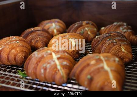 I croissant dorati sono ordinatamente disposti su tavole di legno, insieme ad altri dolci come ciambelle e fette di torta limpida, possibilmente a buffet per la colazione o a un banco da forno. Riprese 4K di alta qualità Foto Stock
