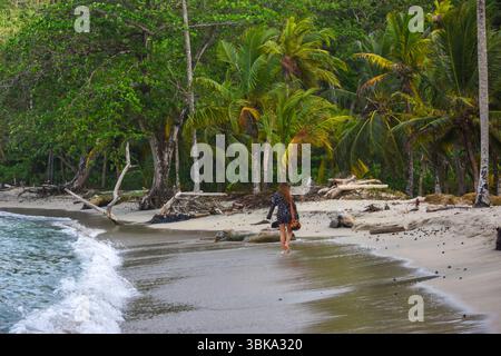 Una tranquilla scena di una donna che cammina lungo la spiaggia di Sapzurro, Choco, Colombia, circondata da lussureggianti palme e dolci onde. Foto Stock