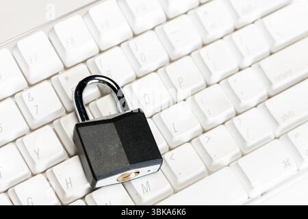 Un lucchetto metallico si trova sulla parte superiore della tastiera di un computer su uno sfondo bianco dello studio, simboleggiando la sicurezza digitale, la protezione dei dati e l'accesso limitato Foto Stock