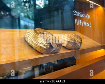 Pani di lievito madre appena sfornati collocati su un ripiano di legno all'interno di una vetrina di panetteria con facciata in vetro e illuminazione calda Foto Stock