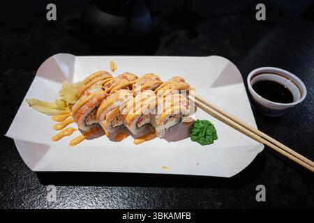 Un sushi roll presentato splendidamente condito con salsa su un piatto di carta moderno Foto Stock