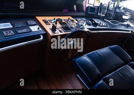 Cabina di pilotaggio per yacht di lusso con cruscotto, vari pulsanti e interruttori, volante, leve di accelerazione e computer di bordo. Cabina di controllo yacht. Foto Stock