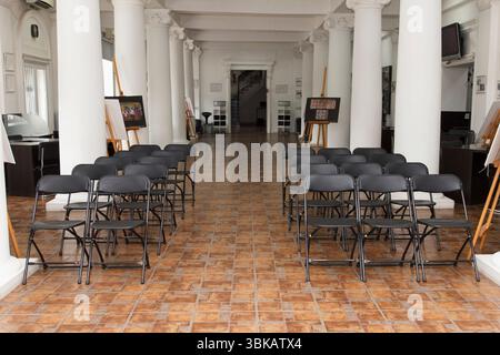 CHISINAU, MOLDAVIA - 14 MARZO 2025; sedie pieghevoli nere vuote disposte in file in una sala con colonne bianche, pavimento piastrellato e opere d'arte incorniciate, rappresentate Foto Stock
