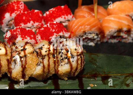Primo piano di sushi roll assortiti con tempura croccante, tobiko e salmone fresco, catturati con luce naturale su uno sfondo scuro Foto Stock