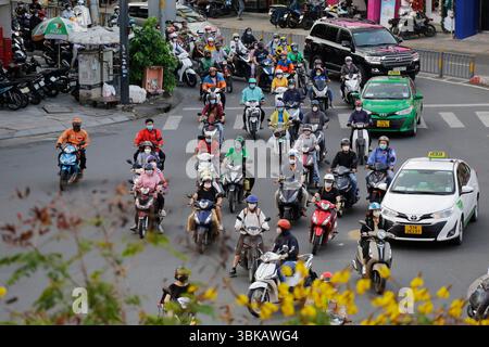 Ho chi Minh City, Vietnam - 8 dicembre 2022: Motociclisti, alcuni dei quali indossano maschere facciali, attraversano un viale a Saigon. Foto Stock
