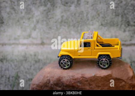 Pick-up giallo in miniatura su terreno roccioso, che rappresenta l'avventura fuoristrada. Scatto ad angolo alto con messa a fuoco morbida, idea creativa di un mondo piccolo. Foto Stock
