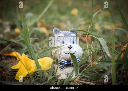 Statuetta di cane in argilla in miniatura con una cravatta tra fiori caduti e erba, catturata in uno sfondo verde macro shot. Tema natura e felicità. Foto Stock