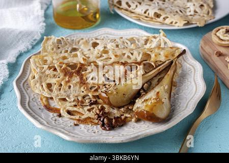 Pancake in pizzo con pere al forno, noci sul tavolo, primo piano Foto Stock