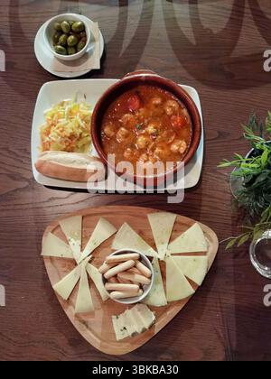 Cubetti di formaggio, gamberi all'aglio, olive verdi. Tapas spagnole tradizionali servite su un tavolo rustico, che mette in mostra vivaci sapori mediterranei perfetti per il tuo soggiorno Foto Stock