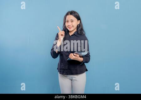 Una donna sorride e tiene in mano un tablet. Indossa una camicia nera e pantaloni bianchi. Concetto di professionalità e fiducia Foto Stock