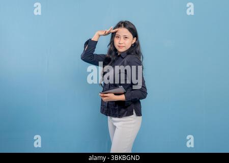 Una donna che indossa una camicia nera e pantaloni bianchi tiene in mano un tablet. Sta guardando in alto e puntando verso il cielo Foto Stock