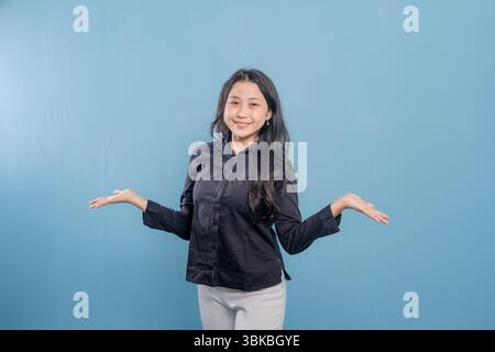 Una donna sorride e alza le mani in alto. Indossa una camicia nera e pantaloni bianchi Foto Stock