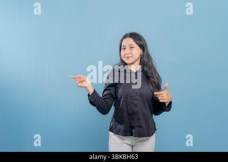 Una donna sta indicando qualcosa con il dito. Indossa una camicia nera e pantaloni bianchi. Lei è sorridente e felice Foto Stock