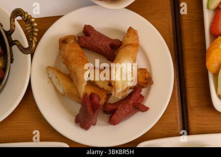 Un tavolo di legno visto dall'alto che presenta un piatto con salsicce fritte e bastoncini di formaggio croccanti, parte di una scena della colazione in hotel. Foto Stock