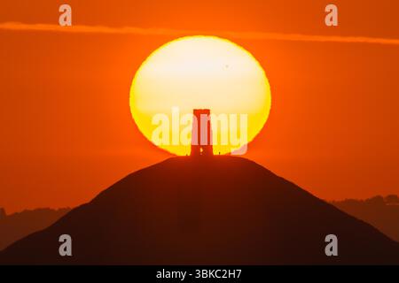 Glastonbury, Somerset, Regno Unito. 20 giugno 2025. Meteo nel Regno Unito. Una spettacolare alba mentre il sole sorge da dietro la St Michael's Tower a Glastonbury Tor nel Somerset in una calda mattina estiva durante l'ondata di caldo. Crediti fotografici: Graham Hunt/Alamy Live News Foto Stock