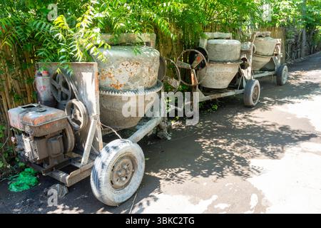 La betoniera con ruota arrugginita si trova in un cortile. La ruota è mancante e la macchina è in riparazione Foto Stock