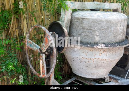 La betoniera con ruota arrugginita si trova in un cortile. La ruota è mancante e la macchina è in riparazione Foto Stock