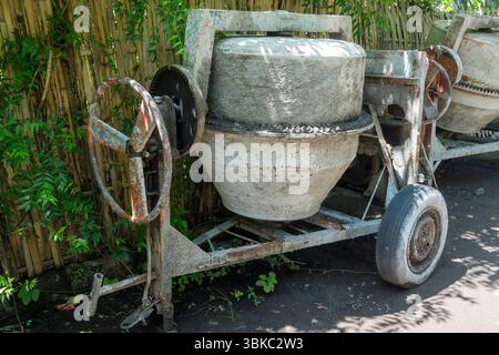 La betoniera con ruota arrugginita si trova in un cortile. La ruota è mancante e la macchina è in riparazione Foto Stock