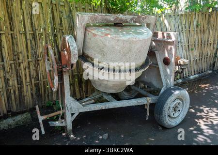 La betoniera con ruota arrugginita si trova in un cortile. La ruota è mancante e la macchina è in riparazione Foto Stock