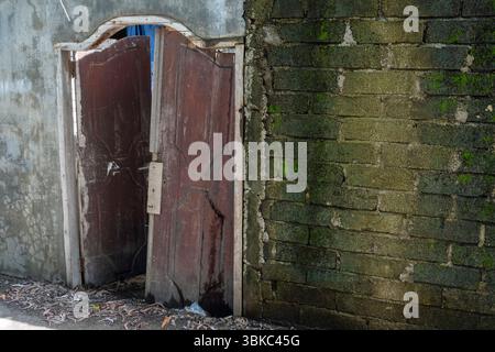 La porta e' aperta davanti ad un muro di mattoni. La porta è vecchia e arrugginita. Il muro è coperto di muschio Foto Stock