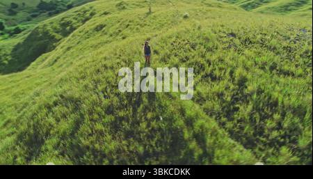 Vista aerea che cattura un'escursionista che attraversa lussureggianti colline erbose sull'isola di Sumba, Indonesia, abbracciando il paesaggio mozzafiato durante una vacanza estiva piena di avventura Foto Stock