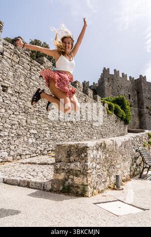 Felice turista che salta con le braccia sollevate vicino allo storico castello di Erice, in Sicilia Foto Stock