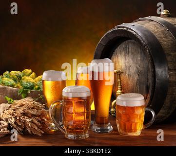 Bicchieri e tazze di birra leggera fredda e botte di birra di legno sullo sfondo. Foto Stock