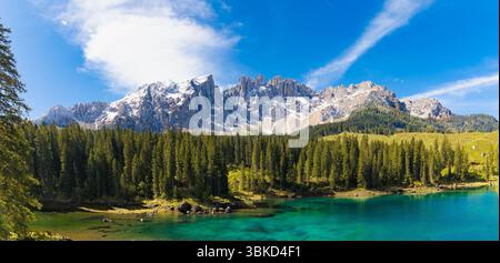Vista panoramica delle splendide acque turchesi del lago di Carezza, una fitta pineta e il maestoso gruppo innevato del Rosengarten nelle Dolomiti. Foto Stock