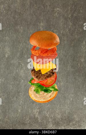 Hamburger volante con i suoi ingredienti pane lattuga pomodori formaggio di manzo salame e cipolle croccanti. Foto Stock
