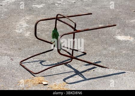 Il vecchio telaio della sedia in metallo arrugginito si capovolge su cemento grezzo, rivestito con un panno verde e circondato da segatura, evocando abbandono e degrado Foto Stock