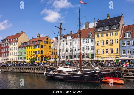La folla si riunisce nella colorata Nyhavn di Copenaghen in una giornata di sole. I turisti salgono a bordo di barche sui canali, acquistano i biglietti e godono di facciate vivaci, atmosfera vivace, Foto Stock