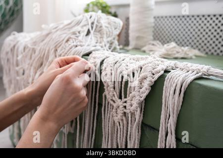 le mani delle donne tessono pannelli in macrame. fili di cotone, filati per la fabbricazione di prodotti fatti a mano per interni. Foto Stock
