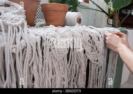 le mani delle donne tessono pannelli in macrame. fili di cotone, filati per la fabbricazione di prodotti fatti a mano per interni. Foto Stock